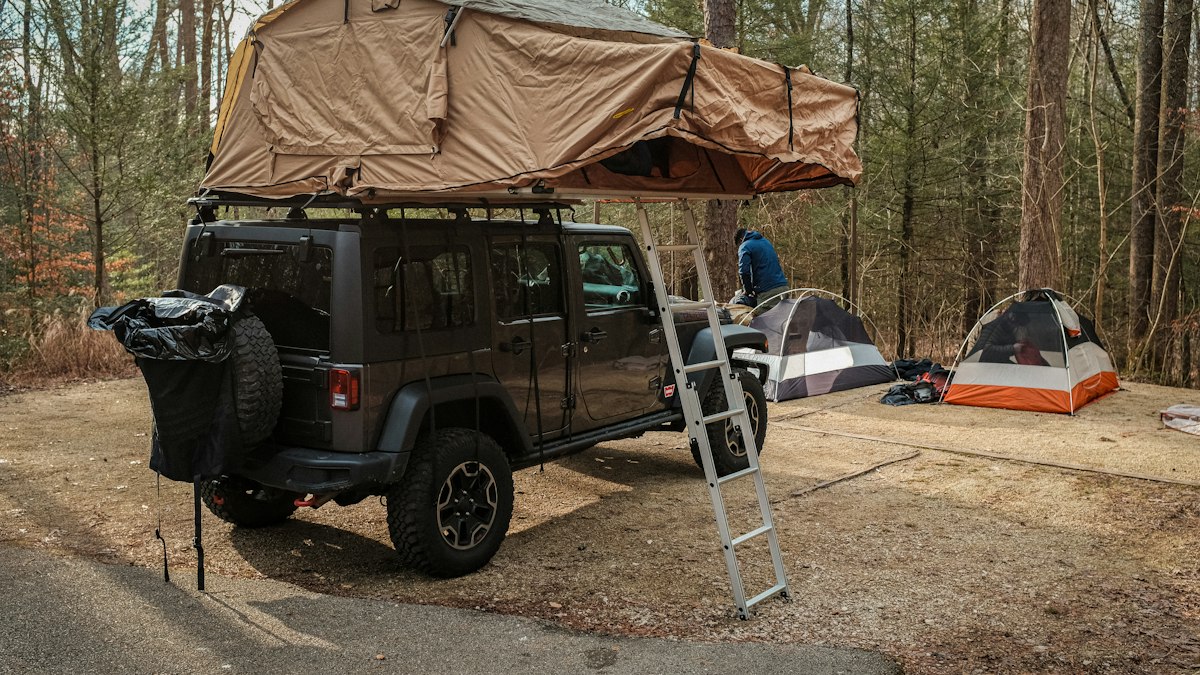 4x4 équipé d'une tente de toit et de son échelle sur un camping en forêt