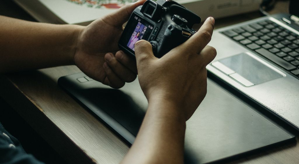 Hands reviewing a photo on a camera screen beside an open laptop